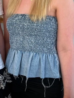 Blå axelbandslös tubtopp med volang - Säljer en blå axelbandslös tubtopp med smockad överdel och volang nedtill. Toppen har en bandeauformad passning och är perfekt för varma dagar. Enkel och stilren design som passar till mycket.