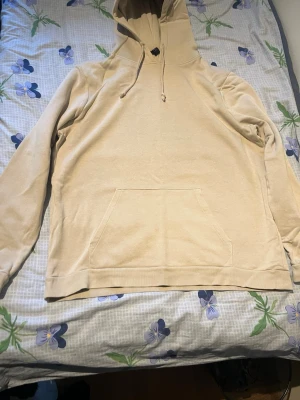Beige hoodie med ficka framtill - Snygg beige hoodie med huva och dragsko, samt en stor känguruficka framtill. Perfekt för en avslappnad och stilren look. Tillverkad i mjukt material som känns skönt mot huden. Passar perfekt till jeans eller joggers.