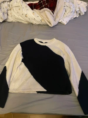 Marinblåvit stickad tröja med mönster - Säljer en stickad tröja i svart och vitt med ett coolt, asymmetriskt mönster. Tröjan har rund halsringning och långa ärmar. Perfekt för dig som gillar en unik och trendig stil.