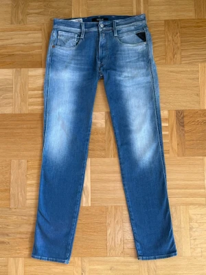 Replay Anbass Hyperflex Blå - Snygga blå jeans från Replay med raka ben och klassisk femficksmodell. Jeansen har en tvättad look med ljusa partier och detaljer som nitar och logotyp på fickan. Tillverkade i mjuk denim som ger en skön passform.