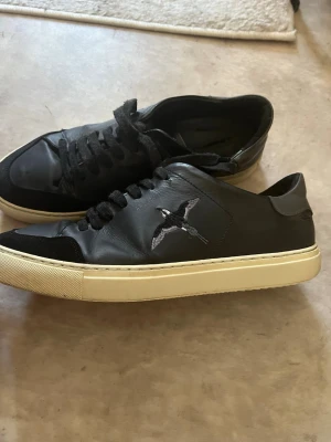 Axel arigato skor  - Ett par snygga Axel arigato skor med en fågel på sidan, använda en del men fortfarande i bra skick. (Säljer dessa åt min kille) 