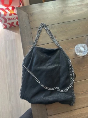 Svart handväska med kedjedetaljer - En Stella McCharty liknande väska(obs ej äkta Stella McCharty) Den är köpt ny pris 700kr. Den är den perfekta vardags väskan och rymmer mycket. 