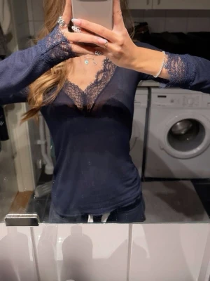 Mörkblå spetsdetaljerad topp - Snygg mörkblå långärmad topp med spetsdetaljer vid v-ringad urringning och ärmslut. Tunn och figurnära modell som ger en elegant look. Perfekt att styla med jeans eller kjol för en trendig outfit. Den är i storlek M men passar mig som vanligtvis har storlek Xs/S. Endast använd 1gång