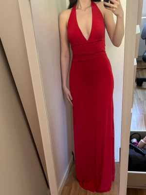 Röd långklänning med halterneck - Snygg röd långklänning med halterneck och djup v-ringning framtill. Klänningen har en figurnära passform och öppen rygg. Jättefin som balklänning. 