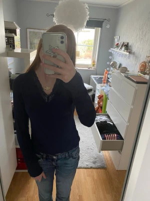 Mörkblå långärmad topp med spets - Mörkblå långärmad topp med v-ringning och dekorativ spetskant runt halsen, liknande den från Intimissimi. Tunn och mjuk i materialet, perfekt för en stilren och enkel look. Passar till alla tillfällen.