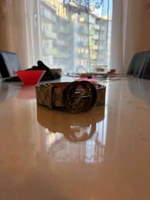 Beige bälte i nytt skick  - Snyggt beige bälte med klassiskt mönster och stor rund metallspänne.. Perfekt accessoar för att lyfta din outfit och ge en exklusiv touch. Bältet har en stilren design och passar till många olika looks. Tveka inte att höra av er vid frågor