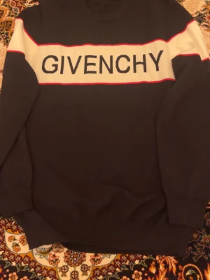 Svart stickad tröja från Givenchy - Hej säljer denna Snygga svarta stickad tröjan från Givenchy. Köpte från annan grabb på vinted för länge sen!  vit panel och röd kant över bröstet där loggan är tydligt insydd. Tröjan har rund halsringning och långa ärmar. Perfekt för dig som gillar exklusiva märken och stilren design.