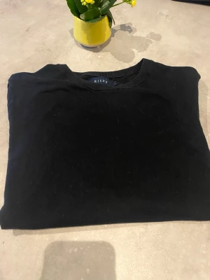 Svart tröja från Riley - En stilren svart tröja från Riley med rund halsringning och långa ärmar. Tröjan har ribbade muddar vid ärmslut och nederkant, vilket ger en snygg passform. Perfekt basplagg till garderoben.