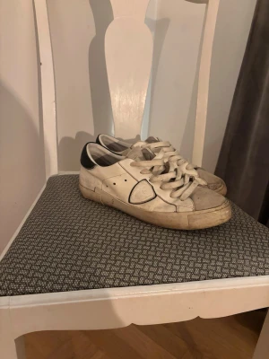 Vita Philippe Model sneakers - Snygga vita sneakers från Philippe Model med svarta detaljer vid hälen och klassisk låg siluett. Skorna har vita snören, diskret logga på sidan och är tillverkade i läder. Perfekta för en avslappnad och trendig stil.