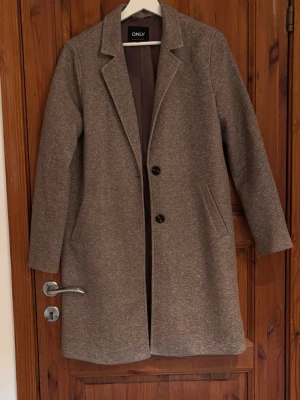 Kappa från ONLY med knappar - Stilren beige/brun kappa från ONLY med klassisk krage och två svarta knappar framtill. Kappan har lång ärm, två fickor och en rak passform. Har använt den ett fåtal gånger så jättefint skick! 🤎