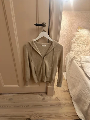 Beige hoodie i kashmir från Soft Goat - Mysig beige hoodie från Soft Goat i mjuk kashmir. Dragkedja framtill, två fickor och ribbade muddar vid ärmslut och nederkant. Klassisk huva med dragsko för extra komfort. Perfekt för en chill och stilren look. Nypris 2900kr