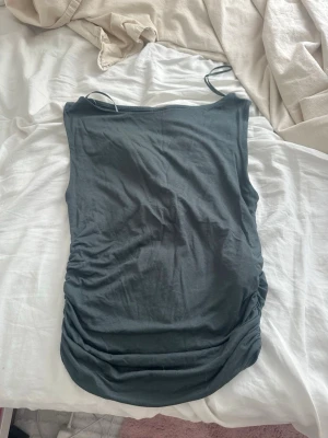 Mörkgrå ärmlös linnetopp - Snygg mörkgrå linnetopp med smala axelband och rynkade detaljer längs sidorna. Toppen är figurnära och har en enkel, stilren design som passar perfekt till jeans eller kjol. Den är typ gröngrå