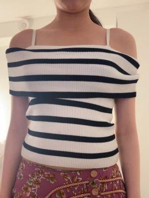 Randig ribbad offshoulder topp - Snygg vit och svart randig topp med ribbad struktur och offshoulder-design. Toppen är figurnära och croppad, perfekt för en trendig look.