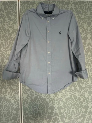 Ralph Lauren skjorta - Säljer denna riktigt schyssta Ralph Lauren skjortan i färgen ljusblå.  Storleken är custom fit - 14, som motsvarar ungefär storlek XS. (Kan fixa mått om ni vill ha)  OBS: skjortan har även en liten defekt på undersidan av högerärmen. Det är inget hål utan bara tyget som slitits lite. (Titta bild 4-5)  Om ni har några funderingar är de bara att fråga!