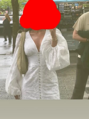 Adoore Vit kort klänning  - Superfin vit kort klänning med v-ringning, puffiga långärmar och knappar framtill. Klänningen har broderade blommor i tyget och markerad midja för en snygg siluett. Perfekt för sommarens alla tillfällen!