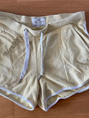 Gula frottéshorts från Lexington i storlek S  - Snygga ljusgula shorts från Lexington i mjuk frotté med vita kanter och snörning i midjan. Storlek S. Perfekta för varma dagar och har en bakficka för extra stilpoäng.
