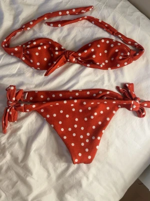 Röd prickig bikini med knyt - Snygg röd bikini med vita prickar och knyt både på toppen och trosorna. Köpte på vinted men passade inte, aldrig använd av mig. Bra skick! Xs/s