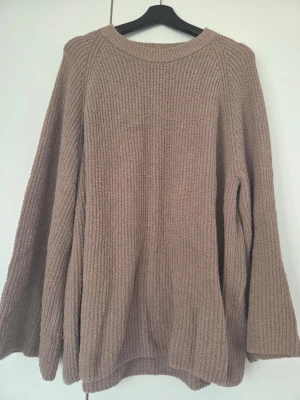 Beige stickad oversized tröja - Mysig beige stickad tröja i oversized modell med rund halsringning och långa ärmar. Tröjan har en grovstickad struktur som ger en avslappnad och trendig look. Perfekt att slänga på sig när det är kyligt ute.
