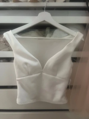 Vit v-ringad croppad topp - Snygg vit croppad topp med djup v-ringning och breda axelband. Toppens form är figurnära och den har en stilren, modern look som passar perfekt till jeans eller kjol.
