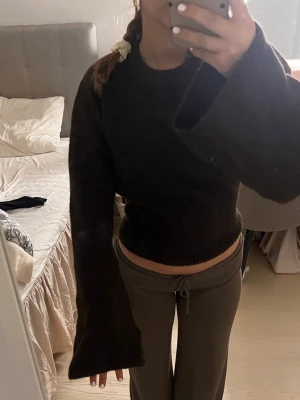 Mörkbrun stickad tröja med vida ärmar - Säljer en mörkbrun stickad tröja med rund hals och extra vida, långa ärmar. Tröjan är croppad och har en figurnära passform vid midjan. Perfekt för dig som gillar en trendig och avslappnad stil.
