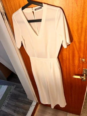 Vit jumpsuit med v-ringning Gina Tricot - Vit jumpsuit från Gina Tricot med korta ärmar, djup v-ringning och vida ben. Jumpsuiten har dragkedja i ryggen och fickor bak. Tillverkad i ett mjukt, lätt tyg som ger en clean och modern look. 
