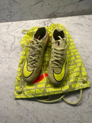 Nike Mercurial Elite - Säljer ett par Nike Mercurial Vapor fotbollsskor i gul och svart med svarta detaljer och snörning. Skorna har en smal, aerodynamisk form och är tillverkade i syntetmaterial för bästa grepp och känsla på planen. Levereras med en matchande Nike-påse som är lite sönder men går att fixa.