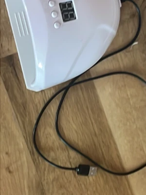 Vit UV-lampa för naglar med USB - Praktisk vit UV-lampa för naglar med digital display och tre knappar för timerinställning. Lampan ansluts via USB-kabel och är perfekt för att härda gelélack hemma. Tillverkad i plast och har en modern, rundad form.