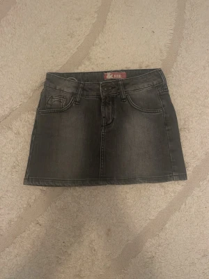 Grå jeanskjol från Now - Snygg grå jeanskjol från Now med klassisk femficksdesign och broderade detaljer på bakfickorna. Kjolen har en kort passform och är perfekt för dig som gillar en avslappnad men trendig stil.💕