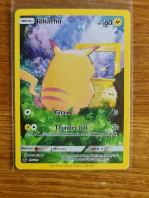Pikachu Pokémonkort 2022 - Pikachu Pokémonkort från 2022 med gul ram och färgglad illustration. Kortet har 60 HP och attacker som Gnaw och Thunder Jolt. Materialet är klassisk glansig kartong och motivet visar Pikachu bakifrån i en skogsmiljö.