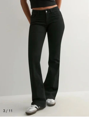 Svarta bootcut jeans från Nelly  - Snygga svarta bootcut jeans från Nelly med klassisk femficksdesign och låg midja. Jeansen har utsvängda ben och stängs med knapp och dragkedja. Perfekta för en trendig och avslappnad stil. Pris kan diskuteras 