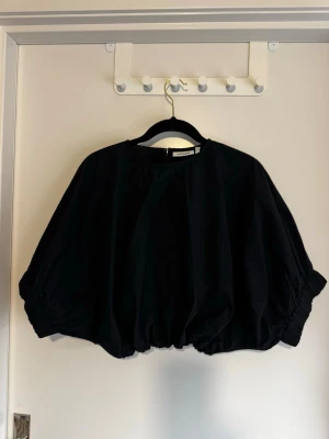 Svart oversized topp från Weekday - Cool svart oversized topp från Weekday med ballongärmar och rund hals. Toppen har en lös passform och elastisk nederkant som ger en unik siluett. Perfekt för dig som gillar statement-plagg och vill sticka ut lite extra. Använd endast en gång.