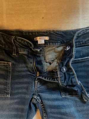 Blå jeans från Gina Tricot bootcut - Säljer ett par blå bootcut jeans från Gina Tricot med dragkedja och knappar framtill. Jeansen har klassiska fickor och är i ett mjukt bomullsmaterial. Perfekta för dig som gillar en avslappnad och tidlös stil.