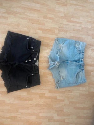 Två par jeansshorts med fransar - Säljer två par snygga jeansshorts, ett par svarta och ett par ljusblå. Perfekta för sommaren. Kan även sälja ett par ifall man skulle vilja det!