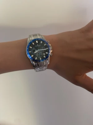 Jacques Lemans silverklocka blå ring - Stilren klocka från Jacques Lemans med silverfärgad länk i rostfritt stål och svart urtavla. Klockan har blå ring runt urtavlan och flera små urtavlor för extra funktioner. Perfekt accessoar för dig som gillar en sportig men ändå klassisk look. Nypris 2000 och jag säljer för mindre än halva priset! 