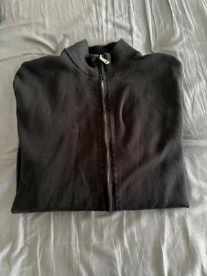 Svart ziptröja med ståkrage - En stilren svart ziptröja med ståkrage och hel dragkedja framtill. Tröjan har långa ärmar och är tillverkad i ett mjukt material som passar perfekt till lager-på-lager. Enkel och klassisk design utan synliga loggor.