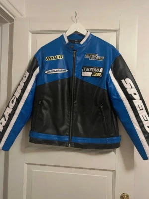 Racing jacka xs - Cool blå och svart skinnjacka med vita detaljer och tryck som 'RACING', 'SPEED', 'TEAM 39' och 'RIDER'. Jackan har dragkedja framtill, två fickor med dragkedja och sportig design inspirerad av racing.