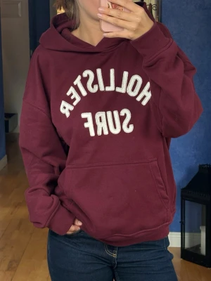Vinröd hoodie från Hollister - Vi röd holister hoodie, med en vanlig ficka fram och en ”gömd” fick med dragkedja i ena sidan 💞