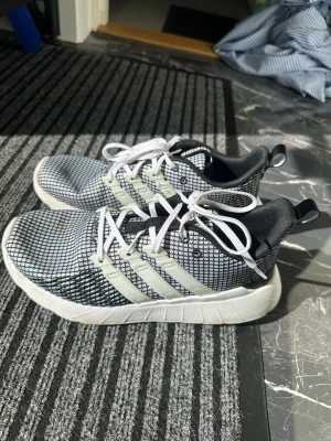 Adidas svartvita sneakers med mesh - Snygga sneakers från Adidas i svart och vitt med mesh-överdel och klassiska tre ränder på sidorna. Skorna har vita snören, svart innersula och en tjock vit sula som ger en sportig vibe. Perfekta för dig som gillar stilrena och bekväma sneakers.