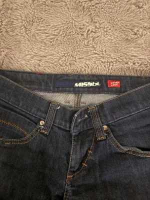 Mörkblå jeans från Miss Sixty strl W29 - Säljer ett par klassiska mörkblå jeans från Miss Sixty med snygga kontrastsömmar och femficksmodell. Jeansen har en normal midja och raka ben. Perfekta för dig som gillar tidlös denim med coola detaljer och en ikonisk logga bak på linningen.