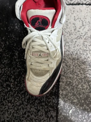 Air Jordan Legacy 312 vit/röd/svart - Säljer en Air Jordan Legacy 312 sneaker i vitt, rött och svart. Skon har högt skaft, klassisk snörning och kardborreband upptill. Ovandelen är i läder och mesh med svarta och röda detaljer samt den ikoniska Jumpman-loggan på plösen.