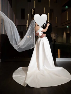 Vit brudklänning med Pärlslöja  - ✨ Elegant bröllopsklänning i satin med off shoulder-design och långt släp. Använd endast 1 gång och är i skick som ny 🤍  Klänningen ger en tidlös och lyxig känsla, perfekt för dig som vill ha en stilren och romantisk look. Lång slöja med pärldetaljer ingår ✨  🤍 Färg: Ivory/vit 🤍 Material: Satin 🤍 Skick: Som ny 🤍 Endast använd 1 gång