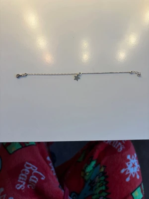 Silveranklet med stjärnberlock - Ett tunt och stilrent anklet i silver med en liten stjärnberlock. Kedjan är enkel och har ett klassiskt lås. Perfekt för dig som gillar minimalistiska smycken med en touch av personlighet.