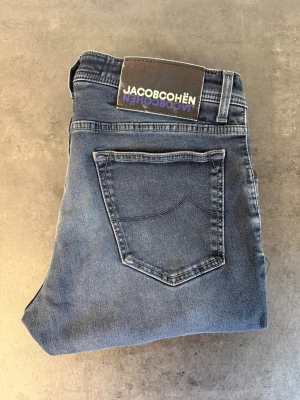 Blå jeans från Jacob Cohën W34 - Snygga blå jeans från Jacob Cohën med klassisk femficksdesign och raka ben. Jeansen har en diskret tvättad look och patch med logga bak i midjan. Perfekta för en avslappnad och trendig stil. Skriv för mått!