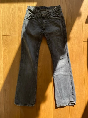Grå lågmidjade bootcut jeans  - Säljer ett par grå jeans med gula detaljer från Denimbirds. Jag säljer pga att de har blivit för små men de är annars jättesnygga. Notera att de är “slitna” i stilen, inte för att de är slarvigt använda! Därför är bild 4 del av designen, inte en defekt. Midje mått tvärs över - 34cm, Innerbenslängd - 78cm