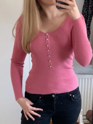 Rosa ribbad långärmad topp - PASSAR ÄVEN STORLEK M! Supersnygg rosa ribbad topp från Zalando med v-ringning och pärl knappar framtill. Långärmad och figurnära passform, perfekt att styla med jeans eller kjol. Mjuk och stretchig i bomullsmix för en bekväm känsla.