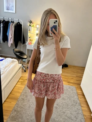 Paisleymönstrade shorts med knyt - Säljer ett par luftiga shorts med paisleymönster i rosa och rött. Shortsen har hög midja och en bred linning med knyt i sidan. Perfekta för varma dagar och ger en söt och trendig look.