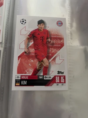 Topps fotbollskort Minjae Kim Bayern - Samlarfotbollskort från Topps med Minjae Kim i Bayern Münchens röda matchställ. Kortet har Champions League-design, spelarens namn, klubbmärke och statistik. Perfekt för samlare av fotbollskort och fans av Bundesliga.