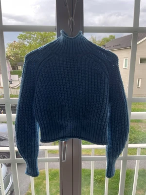 Blå stickad polotröja - Säljer en blå stickad polotröja med grov ribbstickning och lång ärm. Tröjan har en hög krage och är något croppad i modellen. Perfekt för att hålla sig varm och snygg under kyliga dagar. XS 