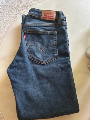 Blå Levi's jeans med klassisk passform - Säljer ett par blå jeans från Levi's med klassisk femficksmodell och vida ben. Jeansen har den ikoniska läderpatchen bak i midjan och röd Levi's-tagg på bakfickan. Perfekta för en avslappnad och tidlös stil.