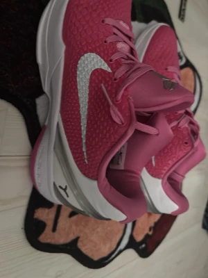  rosa basket sneakers med vit sula - Snygga rosa basket sneakers med vit sula och stor vit logga på sidan. Ovandelen har en texturerad mesh-look och skorna har klassiska skosnören. Perfekta för dig som vill sticka ut med färg och sportig stil.
